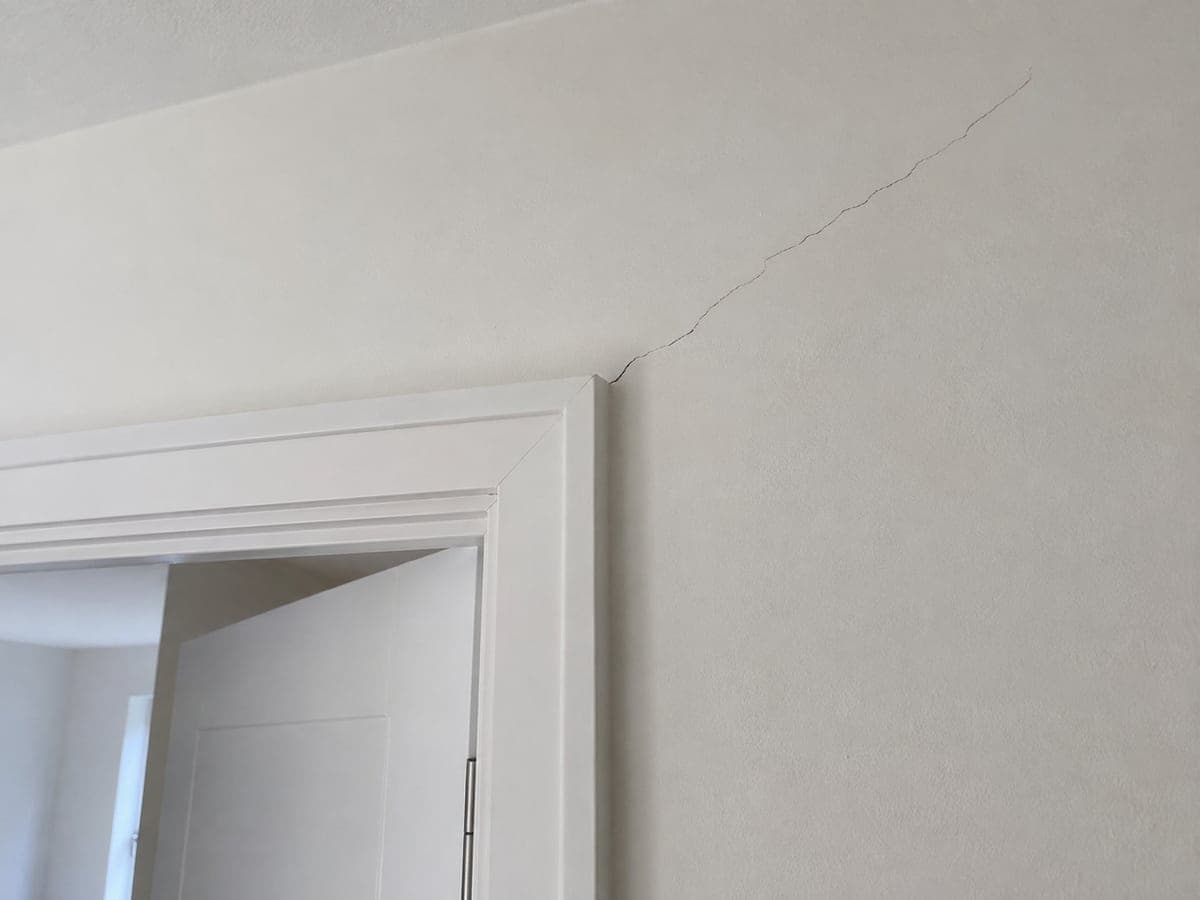 A fine diagonal crack runs through the painted plaster above the upper corner of the door opening.