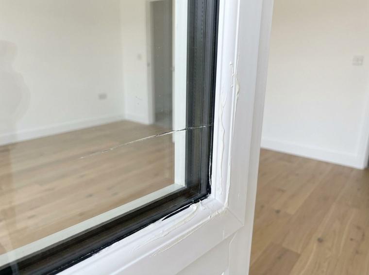 A scratch across the glass of a new double glazed window in a new build, with dried mastic smeared on the white frame bead