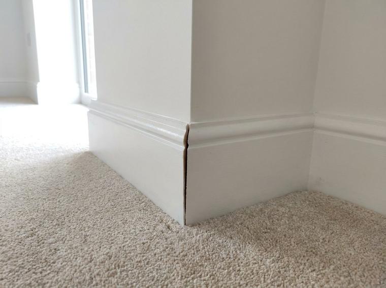 An opened mitre joint between two lengths of new white skirting board in a new build corner, above new carpet